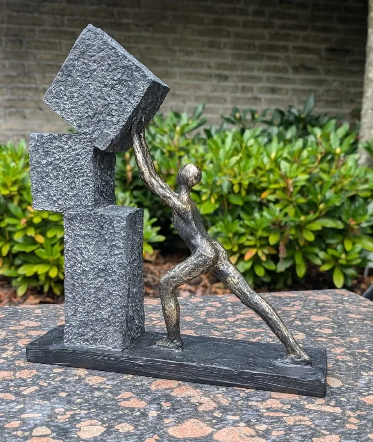 A bronze figure bracing a stack of stone blocks